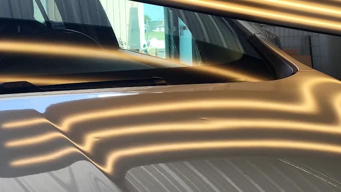 Close-up under reflective light board showing hail dents on a vehicle hood before paintless dent repair