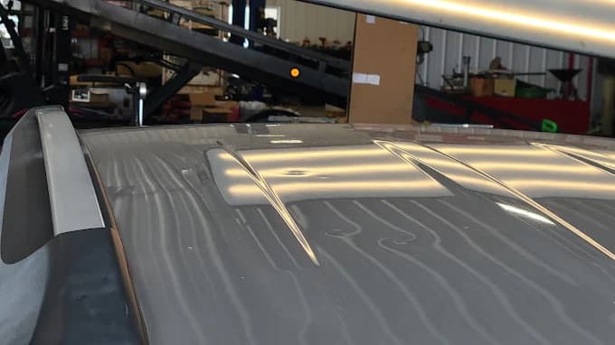 Close-up of vehicle roof under a canopy showing hail damage inspection