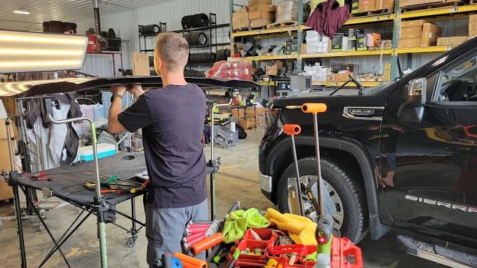 Technician using an LED reflection light board to inspect hail damage on a vehicle roof rail